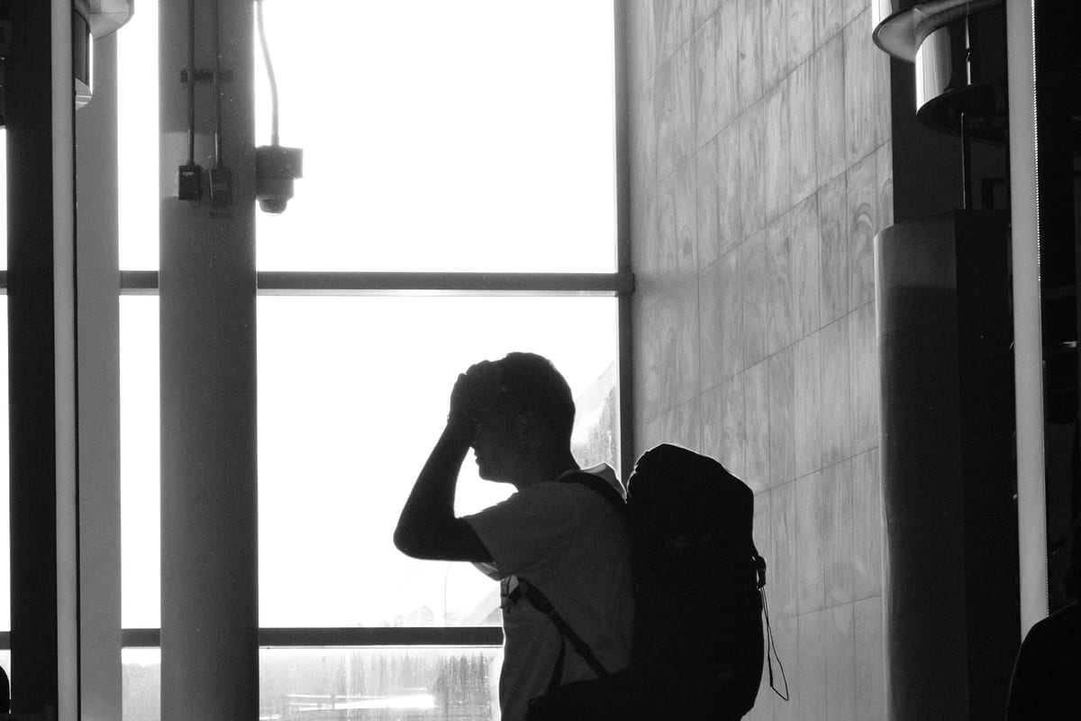 A traveller with a backpack silhouetted against a tall airport terminal window