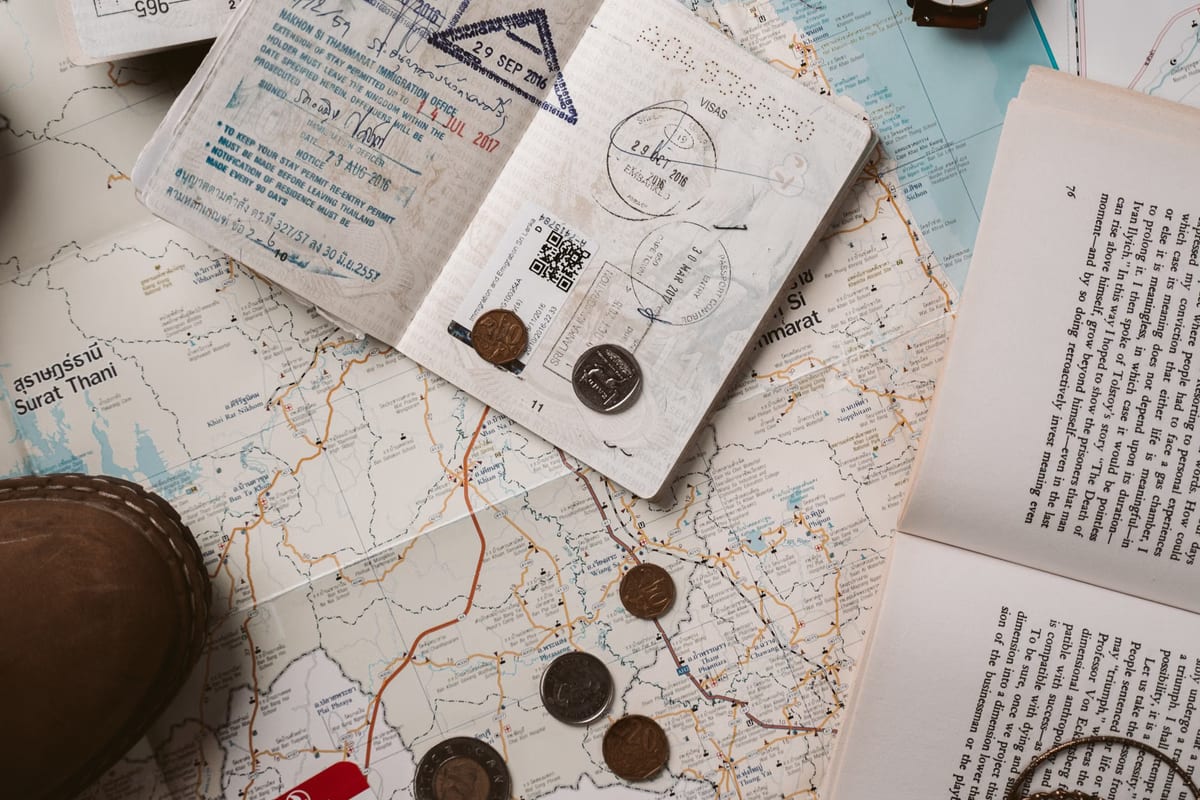 An open passport covered in entry stamps resting on a folded map beside loose coins
