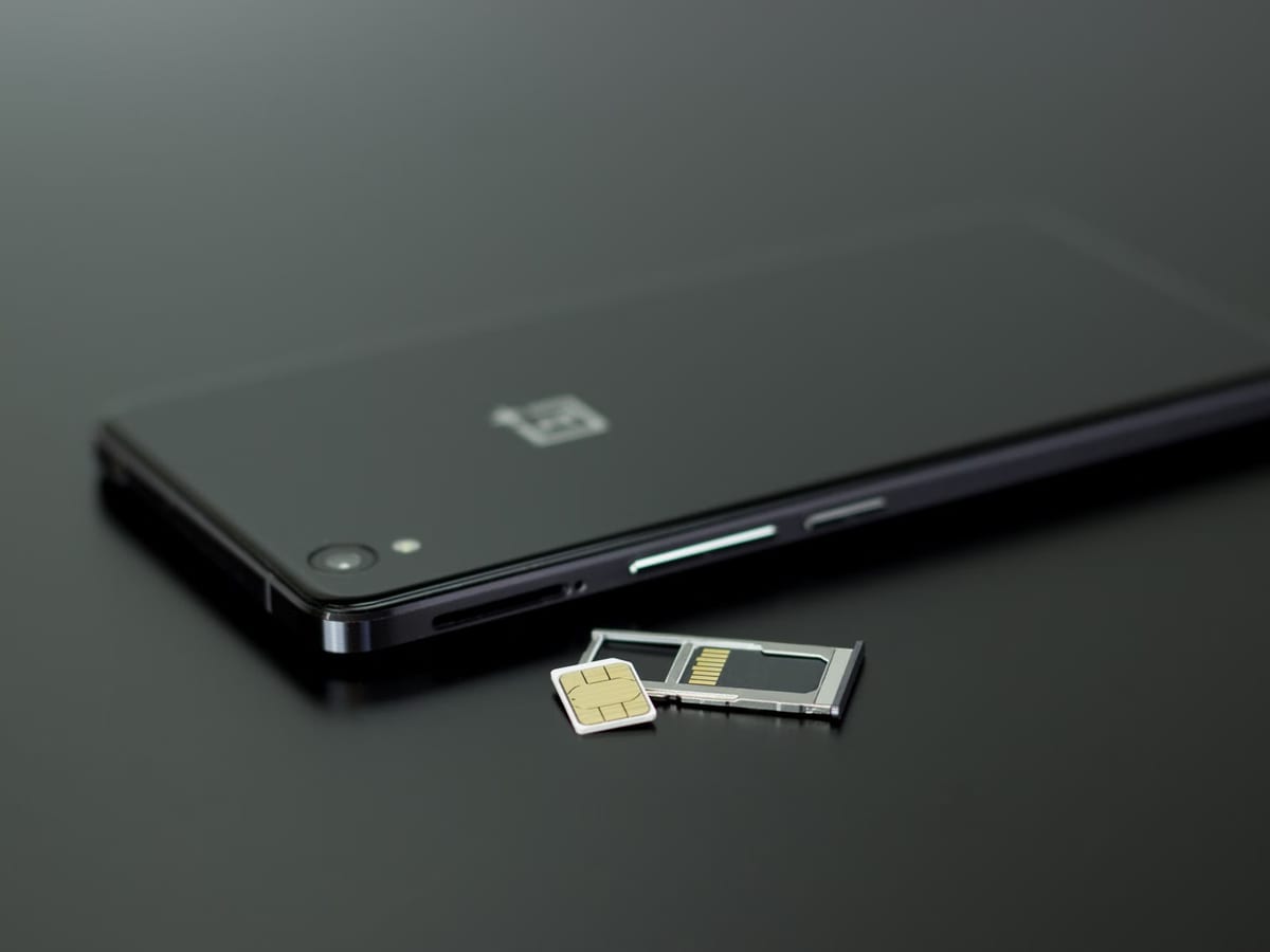 A smartphone on a dark surface with its SIM tray removed and a nano-SIM card beside it