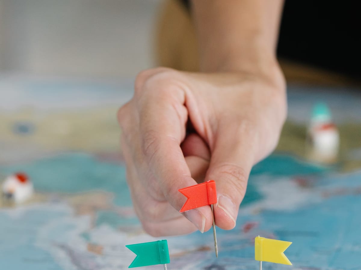 A hand placing small coloured flags into a map to mark destinations